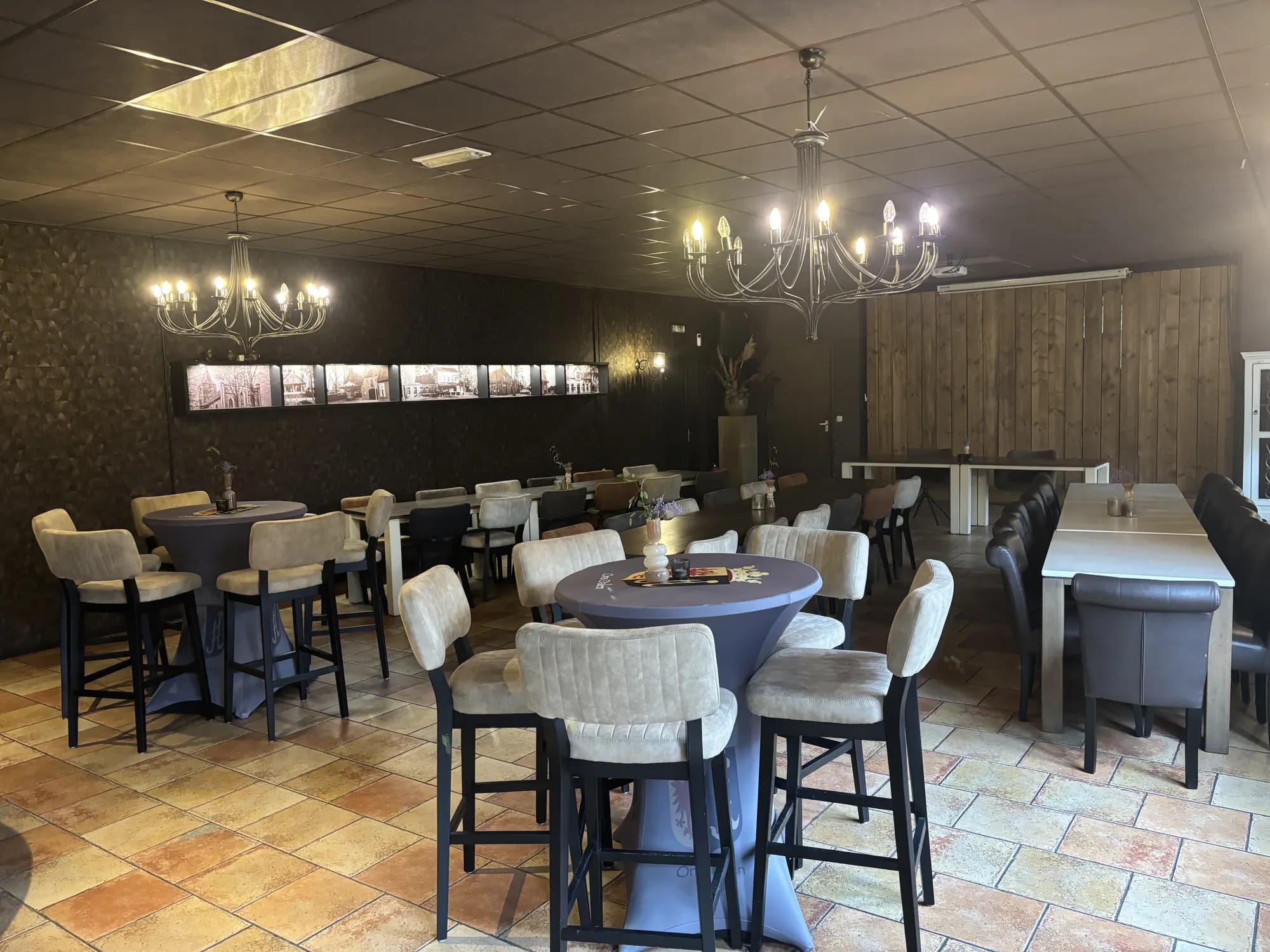 Feestzaal met statafels, barkrukken en kroonluchters, ingericht voor een borrel of feest