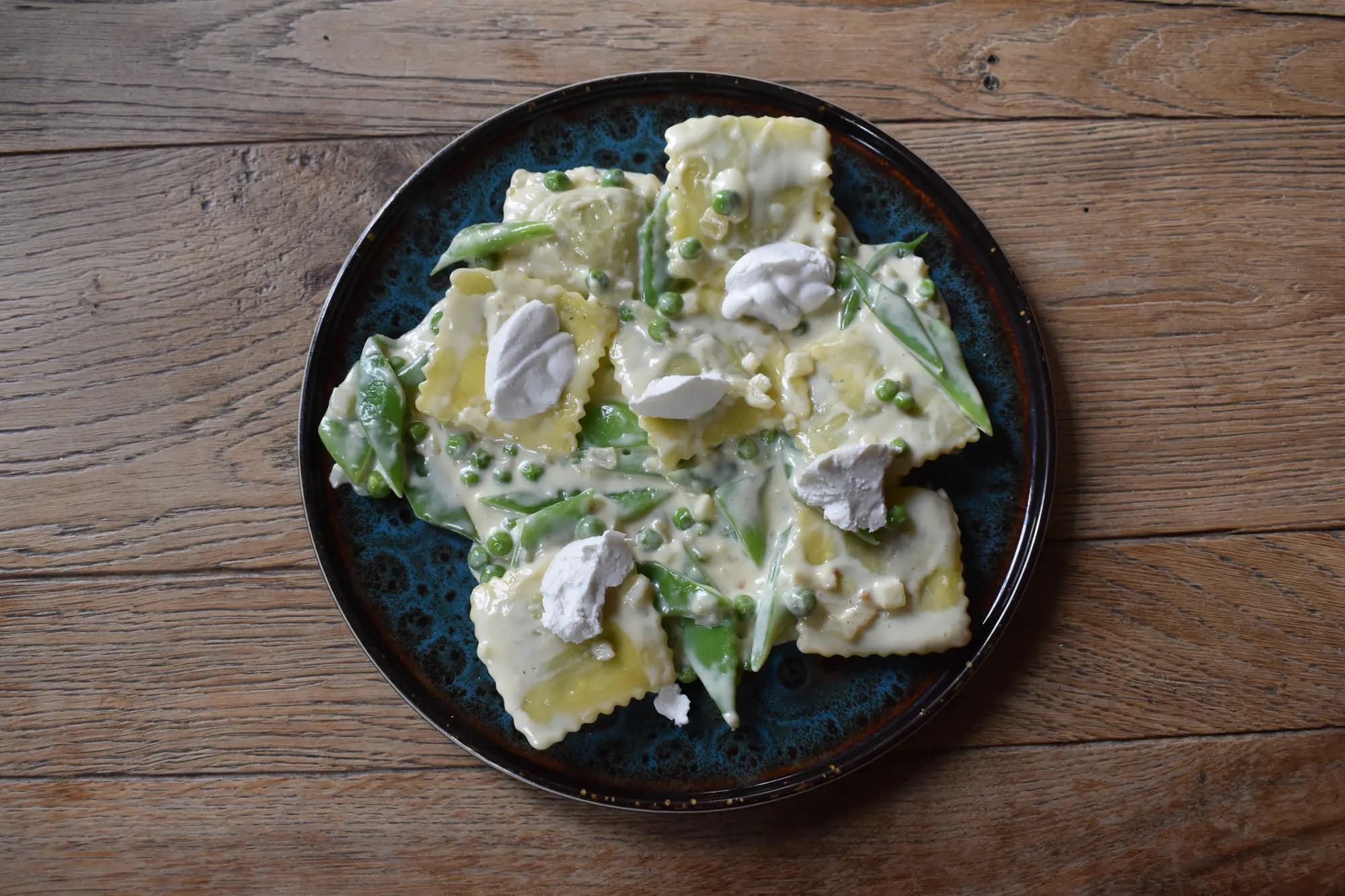 Ravioli met doperwten, peultjes en roomsaus, afgewerkt met vlokken op een blauw bord