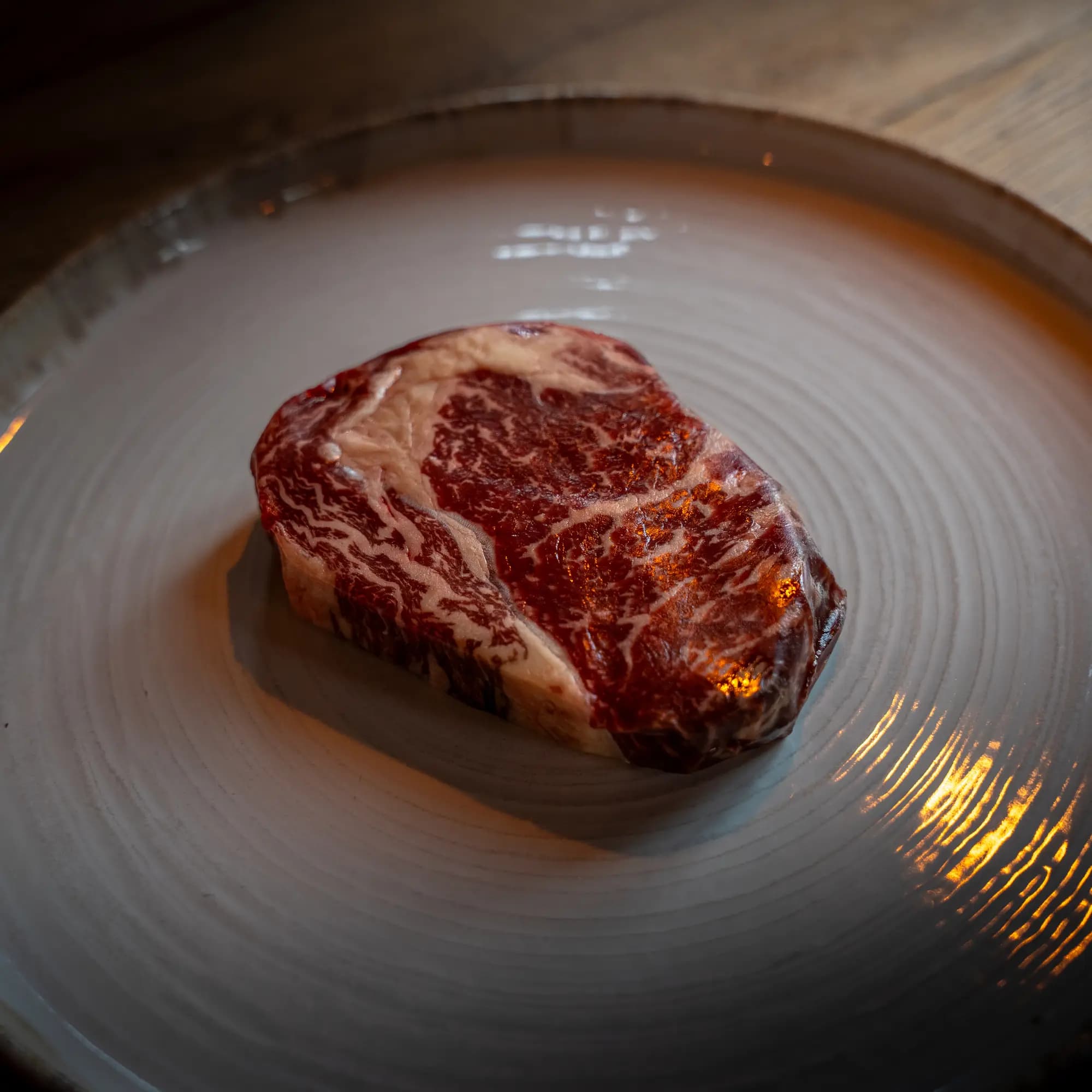 Rauwe dry-aged ribeye met fijne vetmarmering op een licht keramisch bord