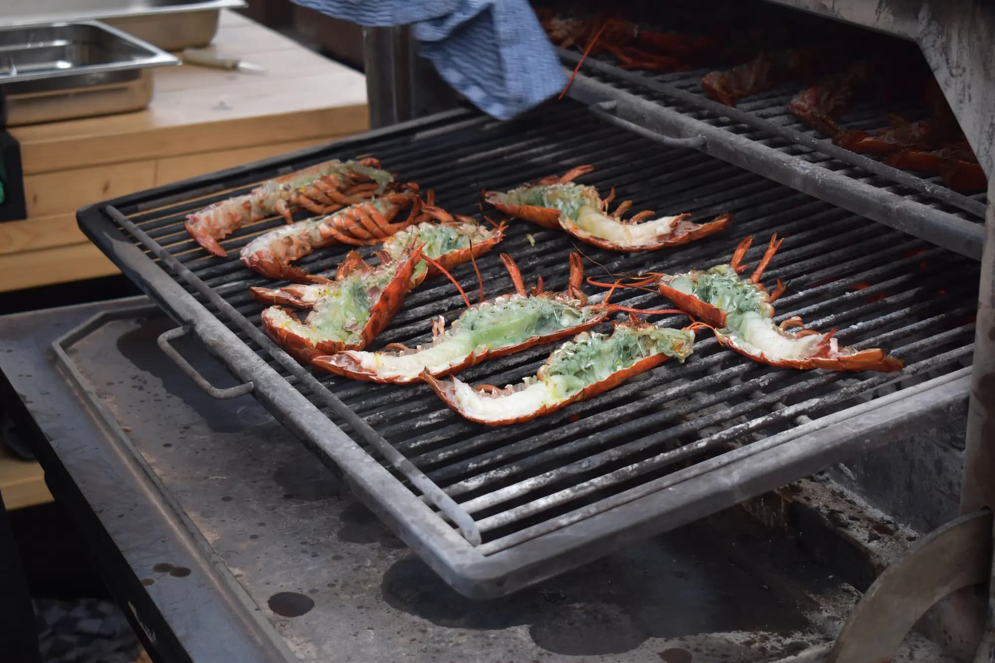 Gehalveerde kreeften met kruidenboter liggen te garen op een grote houtskoolgrill