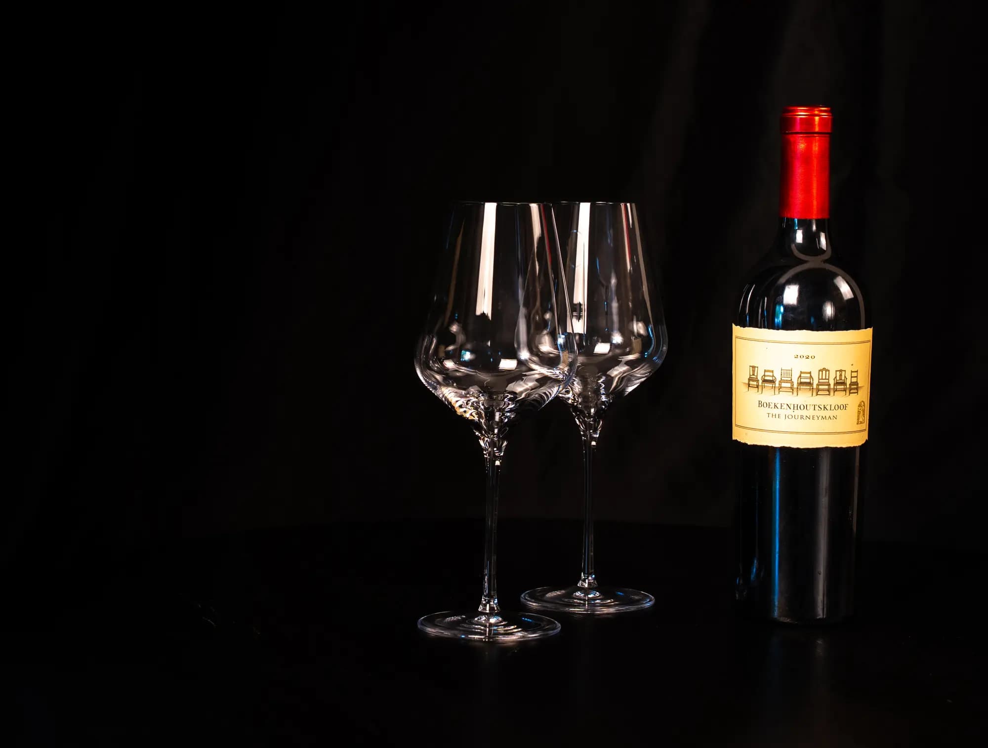 Fles rode wijn naast twee lege wijnglazen tegen een zwarte achtergrond