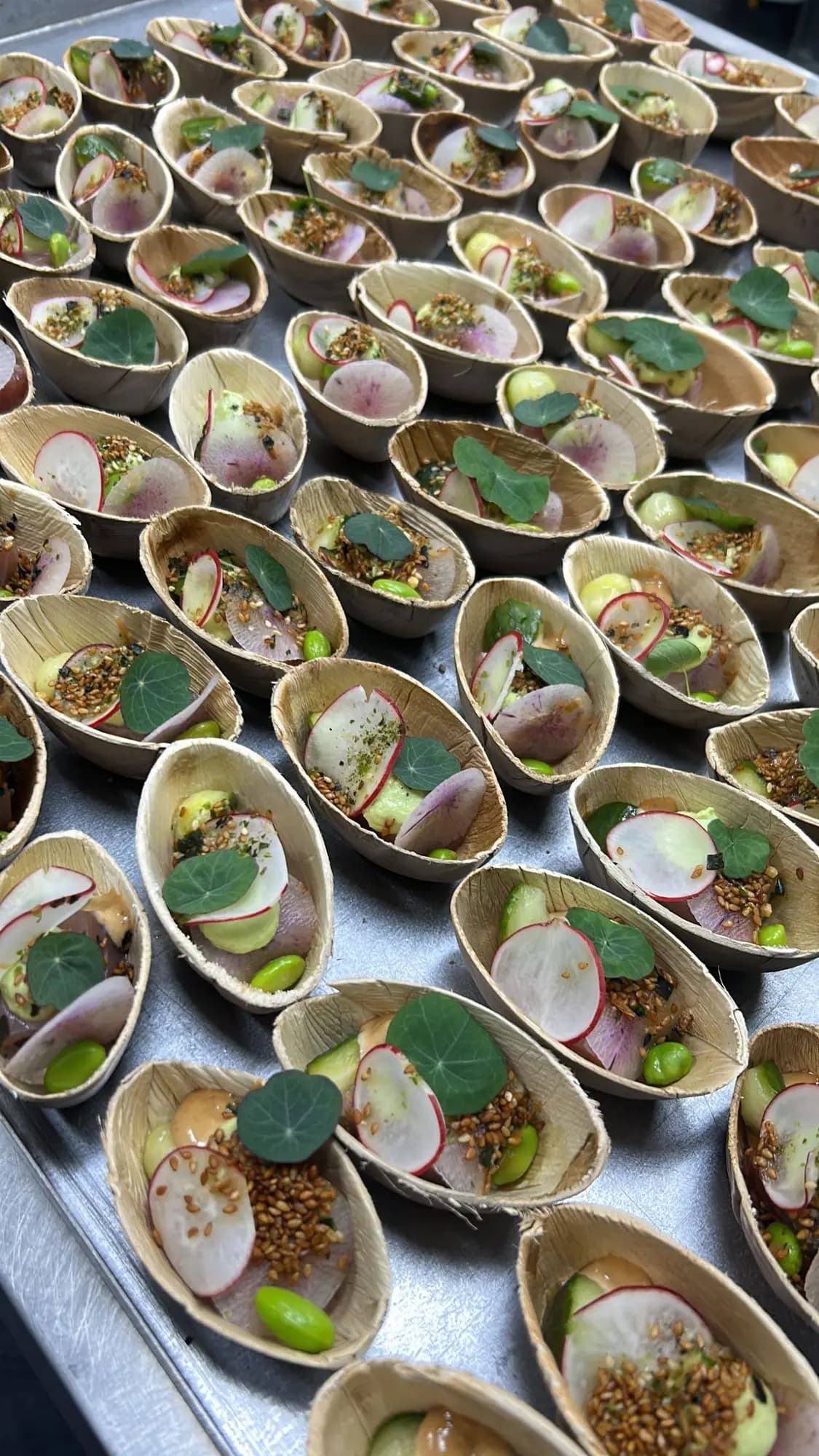 Amuses in palmbladbakjes met radijs, edamame en oost-indische kers op een serveerplaat