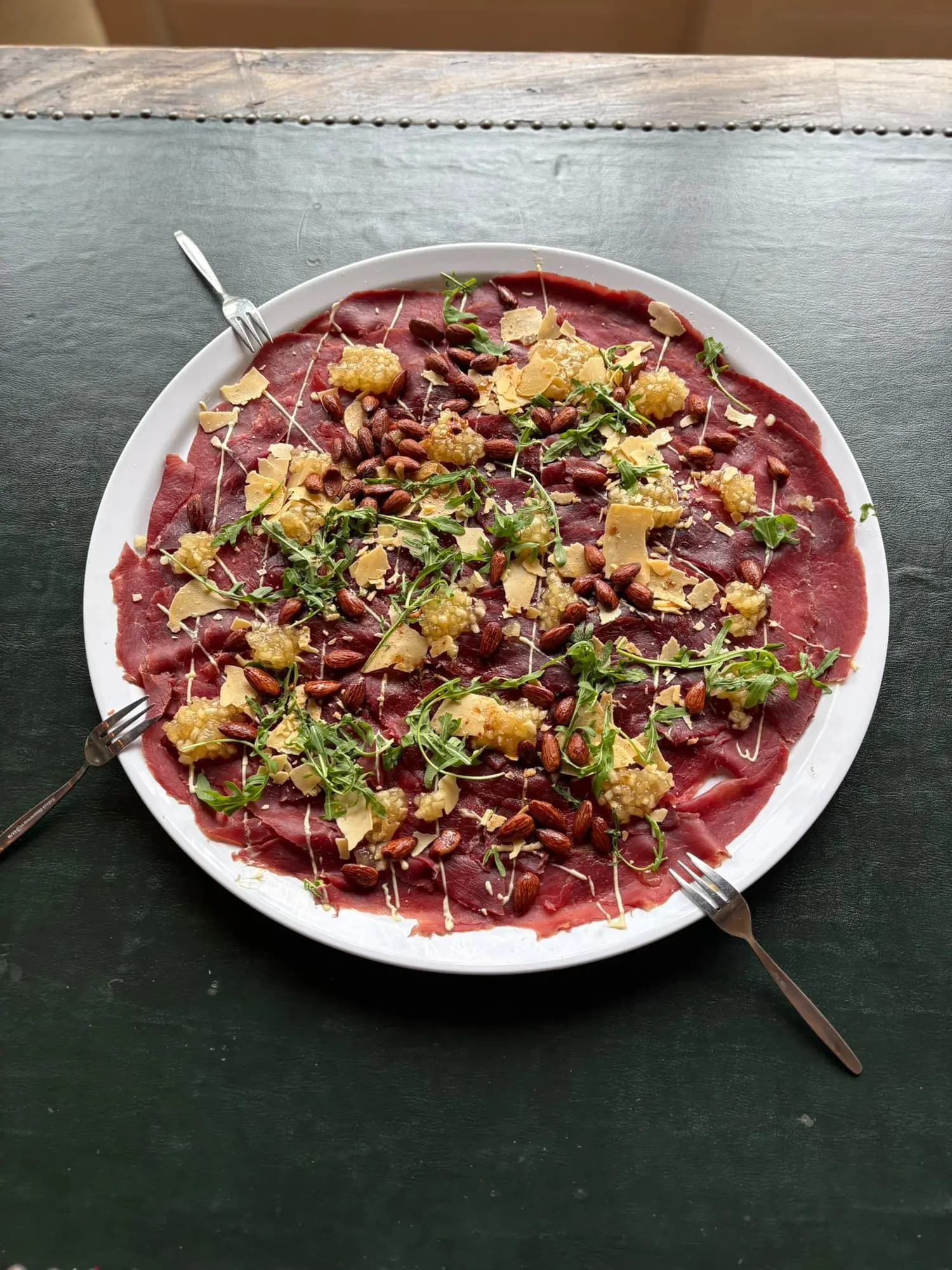 Carpaccio met rucola, oude kaas, geroosterde amandelen en dressing op een ronde schaal