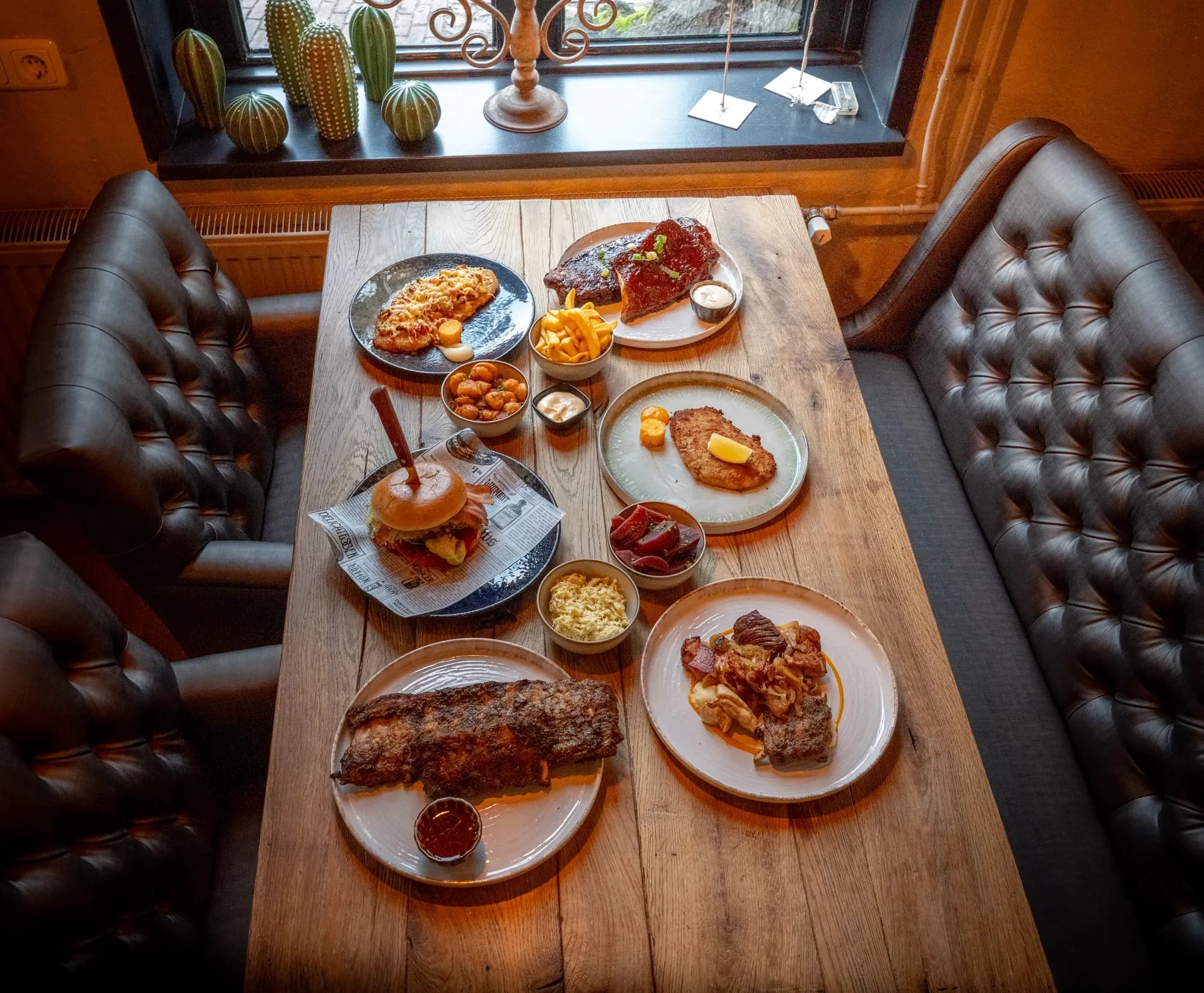 Bovenaanzicht van een tafel vol lunchgerechten: burger, spareribs, friet en sausjes