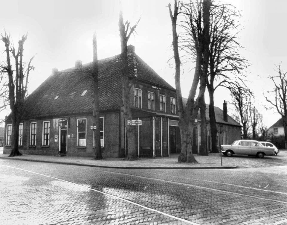 Zwart-witfoto van het pand van de Baander in de jaren '70, met een oldtimer op de natte kasseienstraat